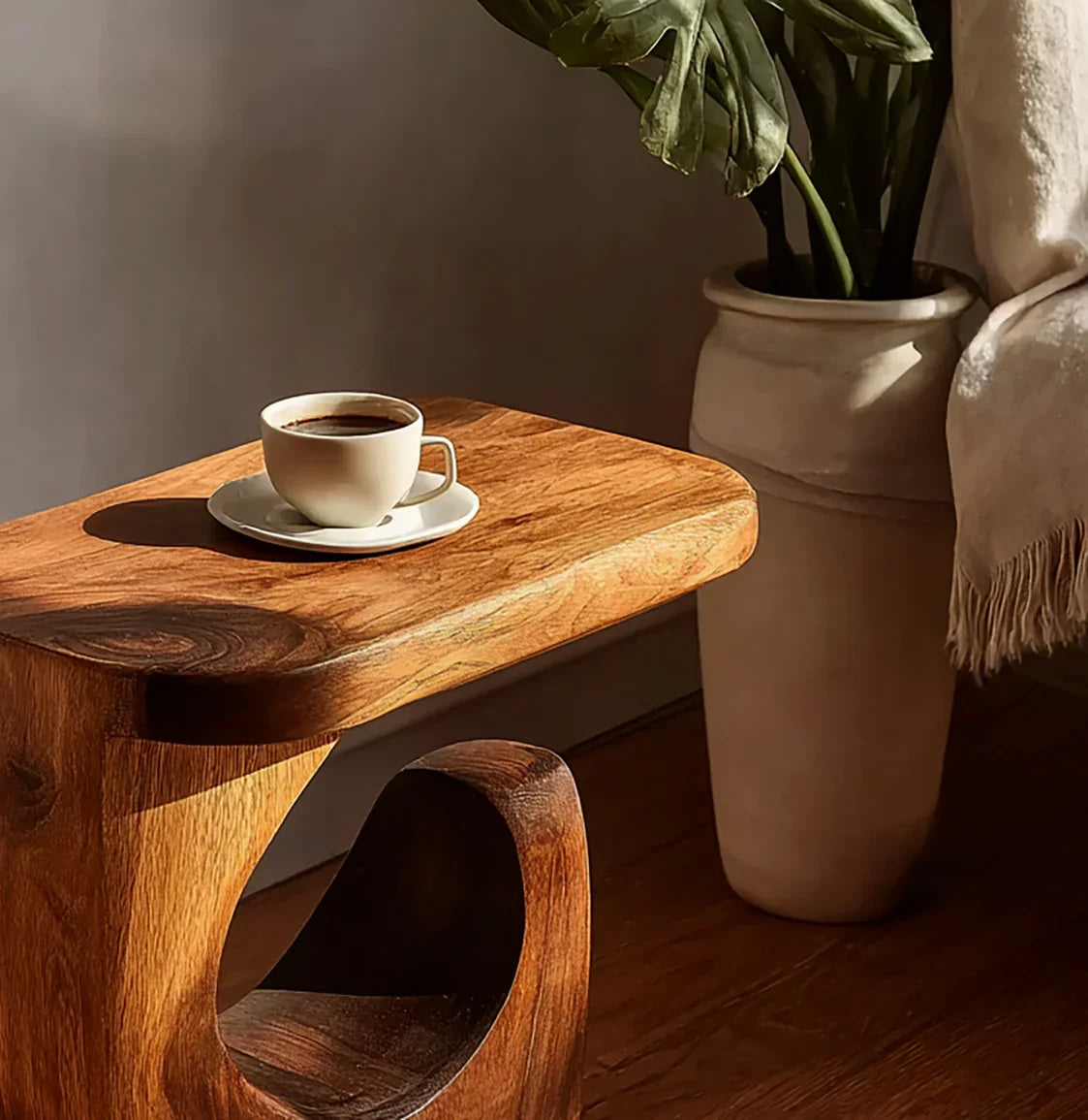 Cup of black coffee on a wooden side table next to a large ceramic plant pot with green leaves