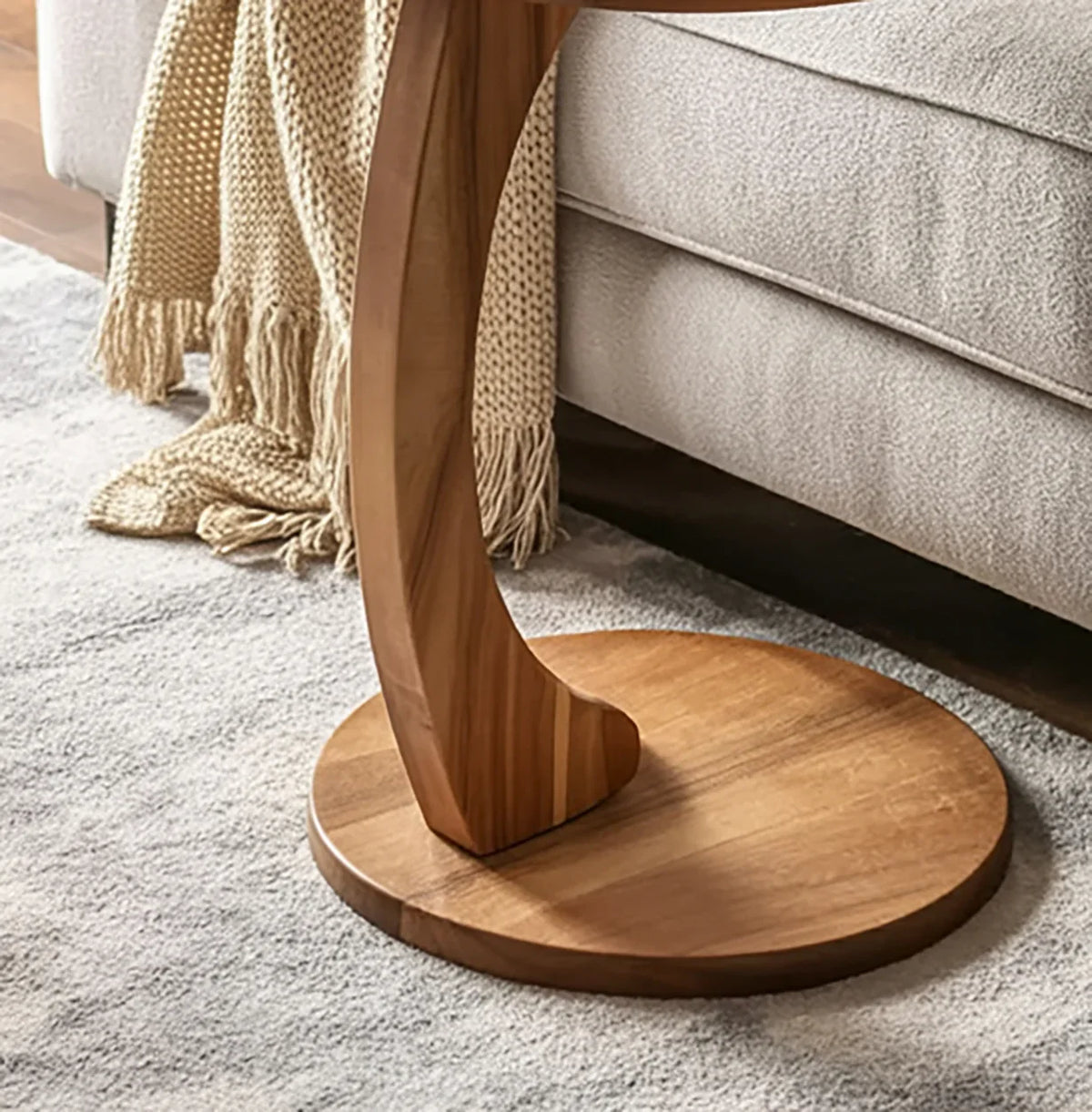 Solid wood side table with curved base on a rug, next to a sofa and knit throw blanket