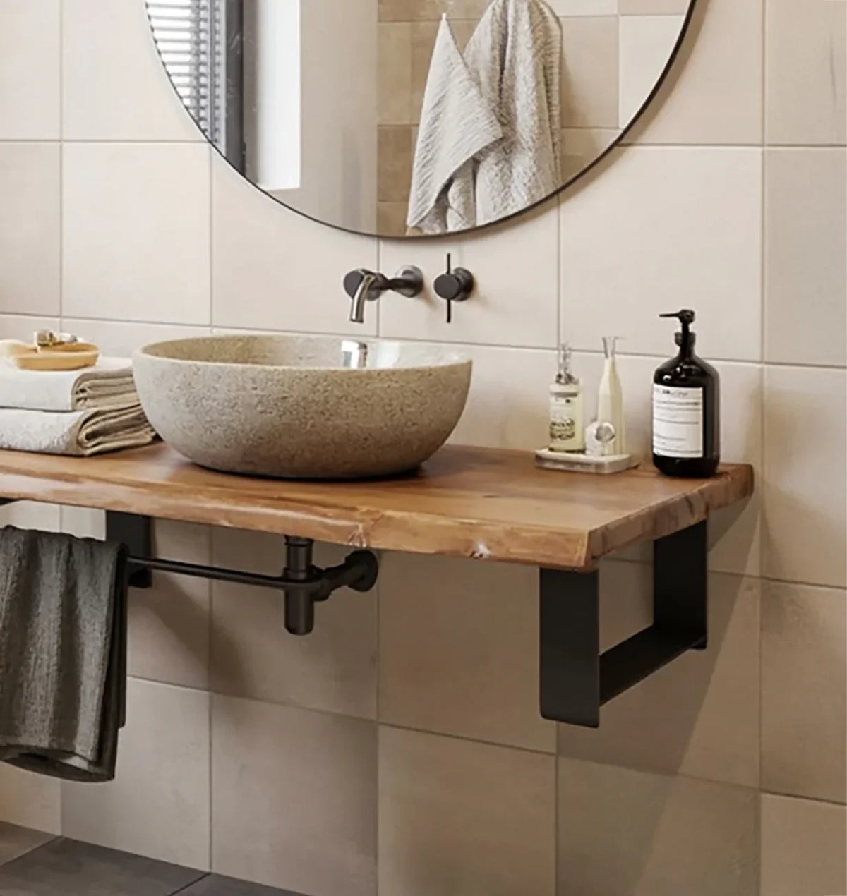 Modern bathroom with stone vessel sink on wooden countertop, round mirror, and wall-mounted faucet