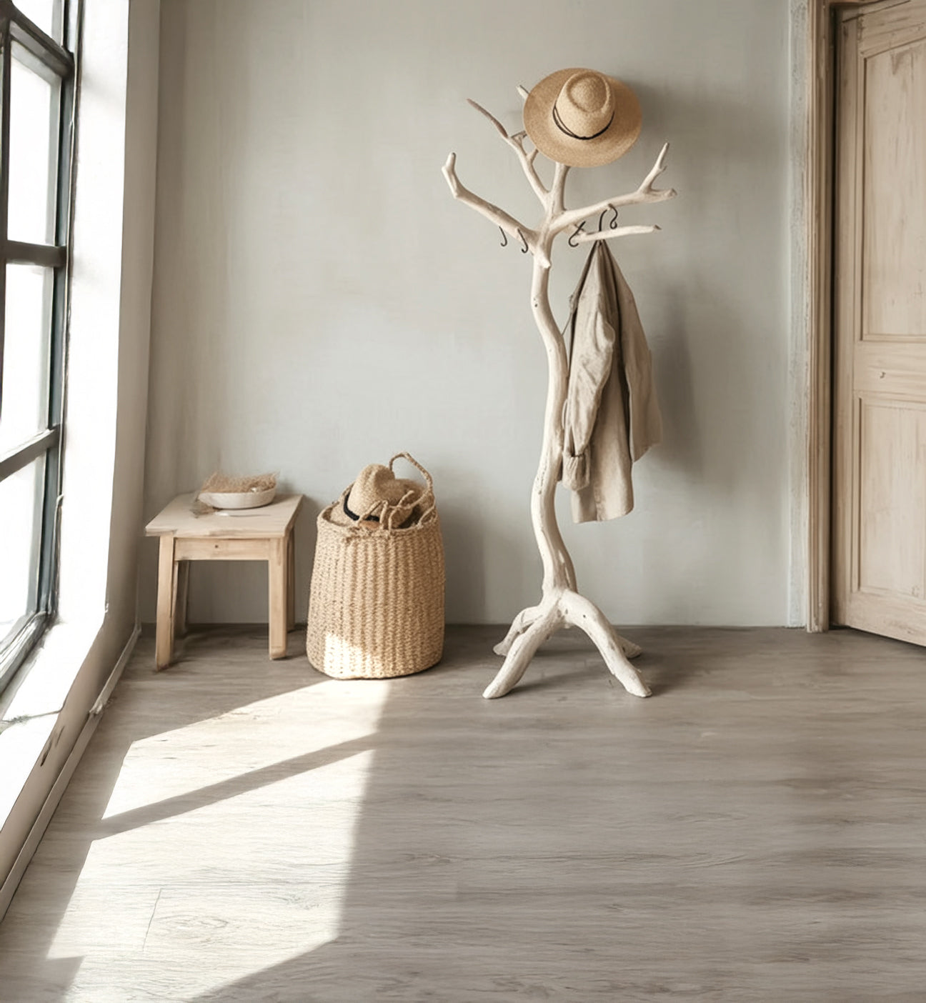 Minimalist entryway with rustic wood coat rack holding coat and straw hat beside wicker basket and wooden stool