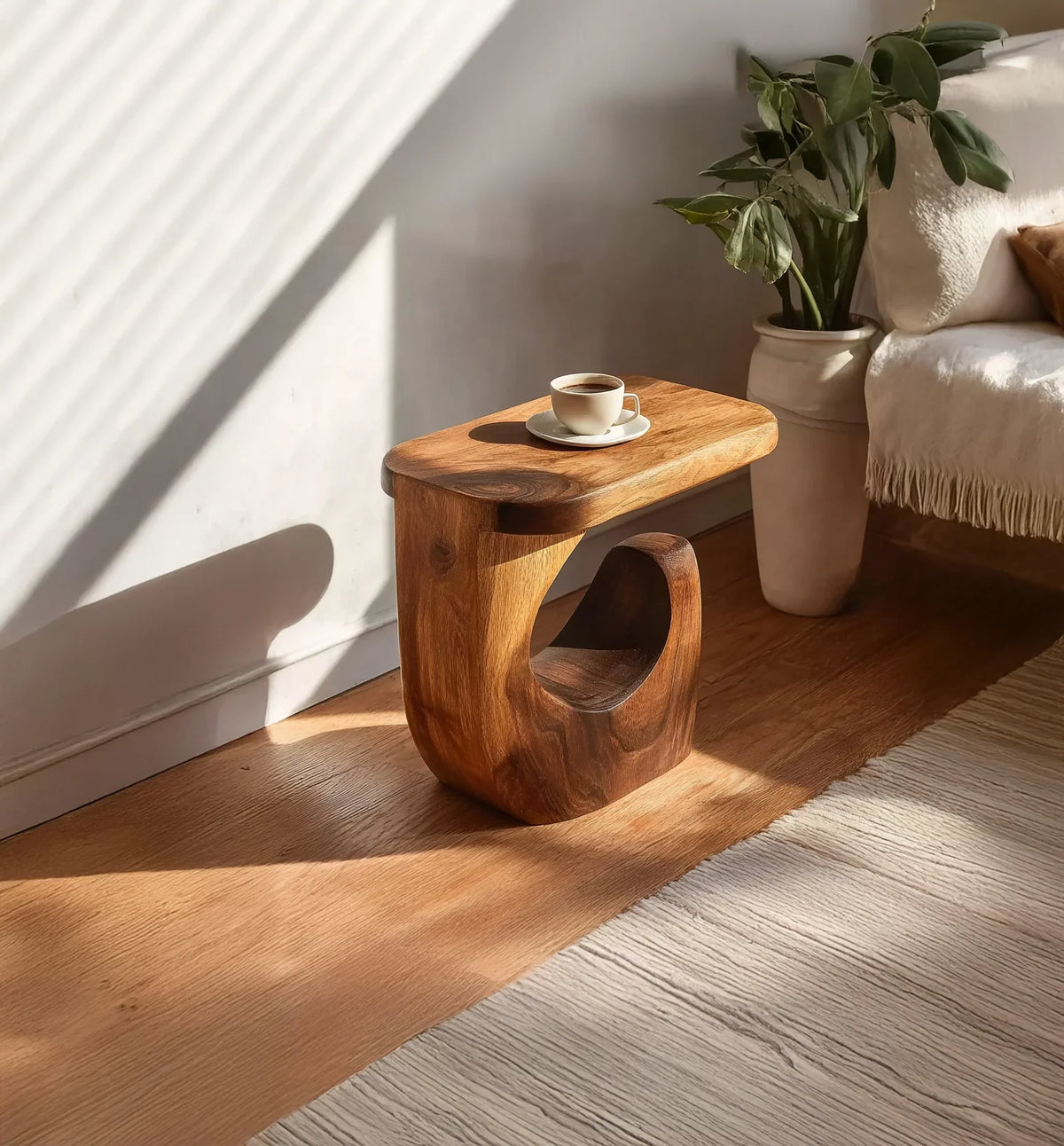 Modern wooden side table with cup of coffee, sunlight, plant in pot, cozy living room decor