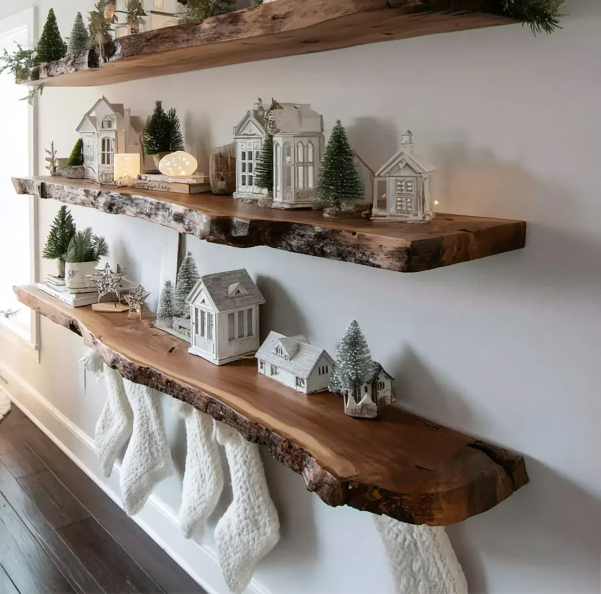 Rustic live edge wood shelves decorated with white Christmas village houses, bottle brush trees, and hanging knit stockings