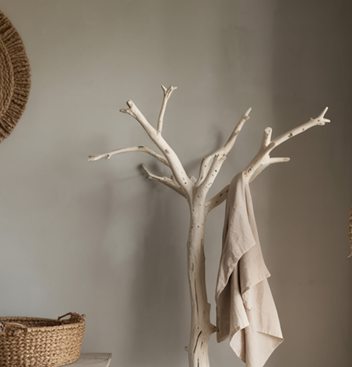 Minimalist beige wooden coat rack with a beige cloth hanging, next to woven basket and neutral wall
