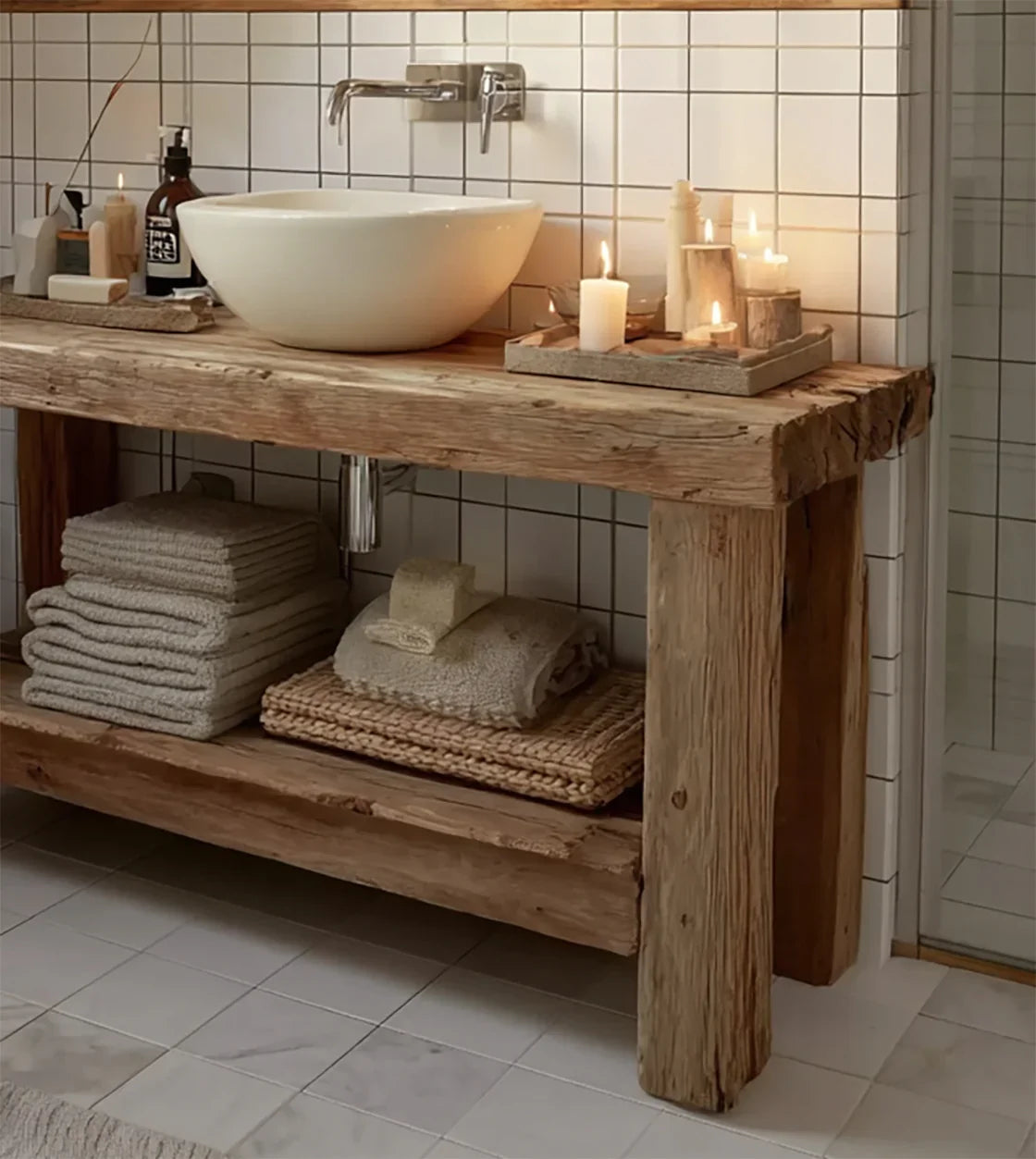 Rustic wooden bathroom vanity with white vessel sink, lit candles, towels, and white tiled wall