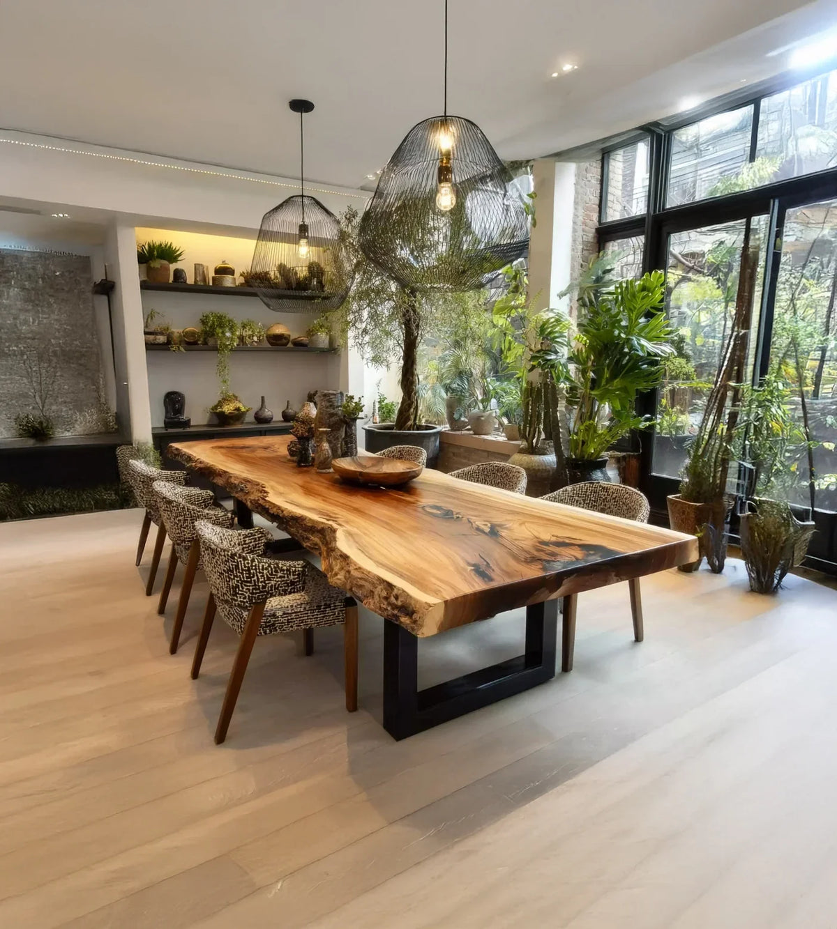 Modern dining room with live edge wood table, patterned chairs, black pendant lights, and lush greenery