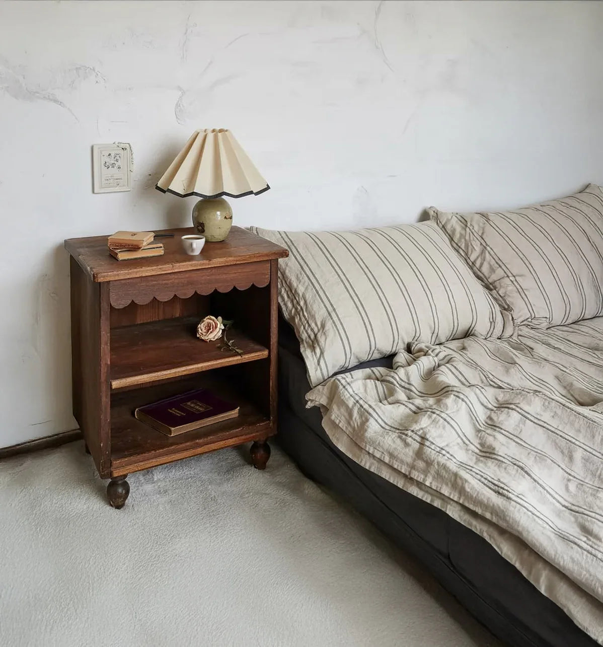 Wooden nightstand with vintage lamp and books beside a striped bedding bed