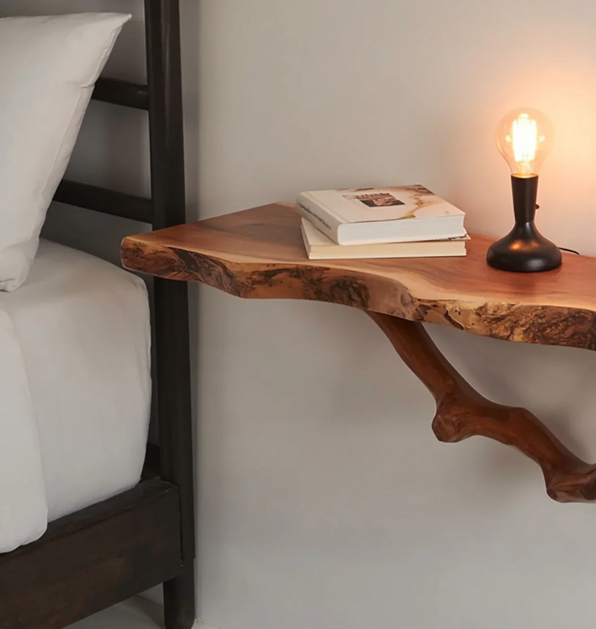 Live edge solid wood floating nightstand with a lamp and books beside a bed