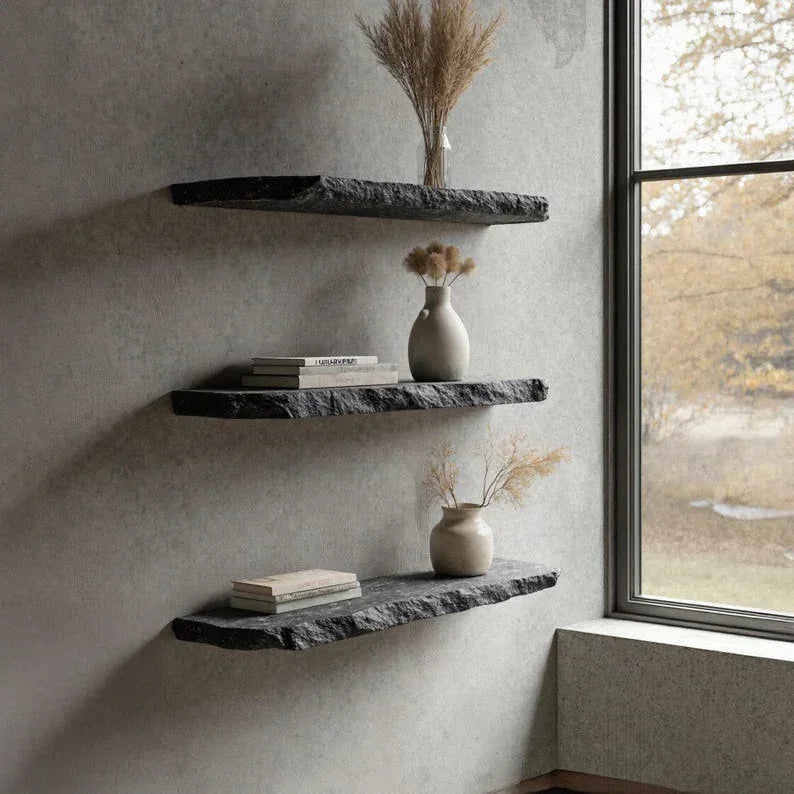 Three black live edge floating shelves with vases and books on a gray wall by a window