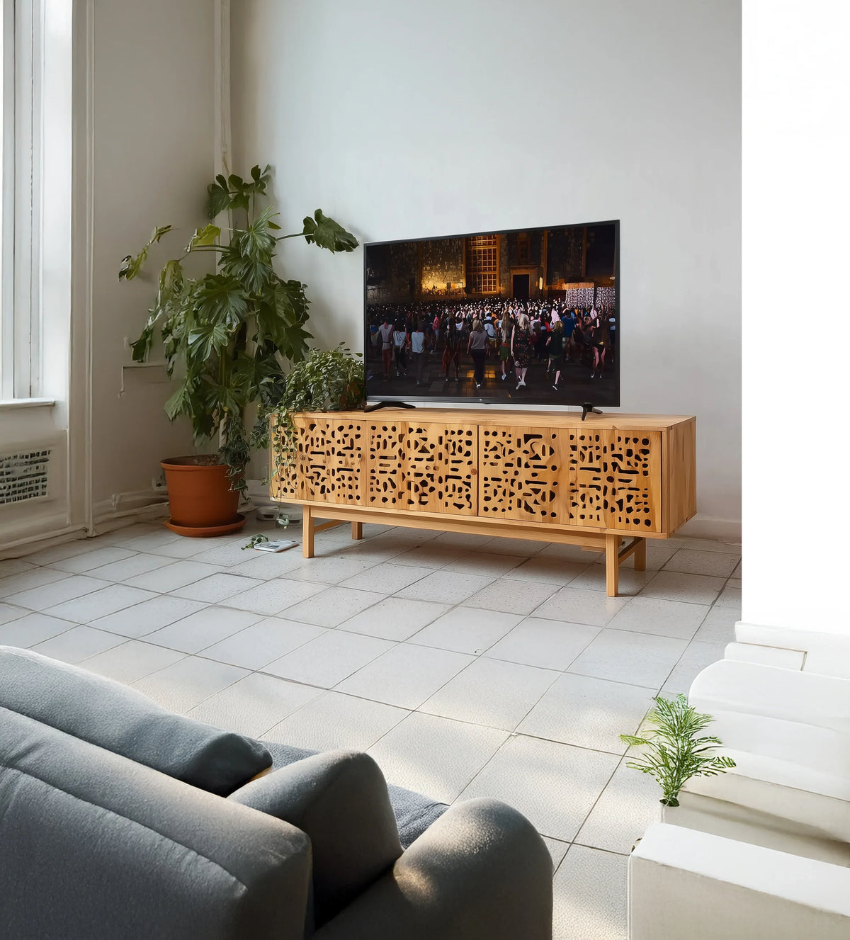 Modern living room with large potted plant, TV on carved wood media console, light tile floor