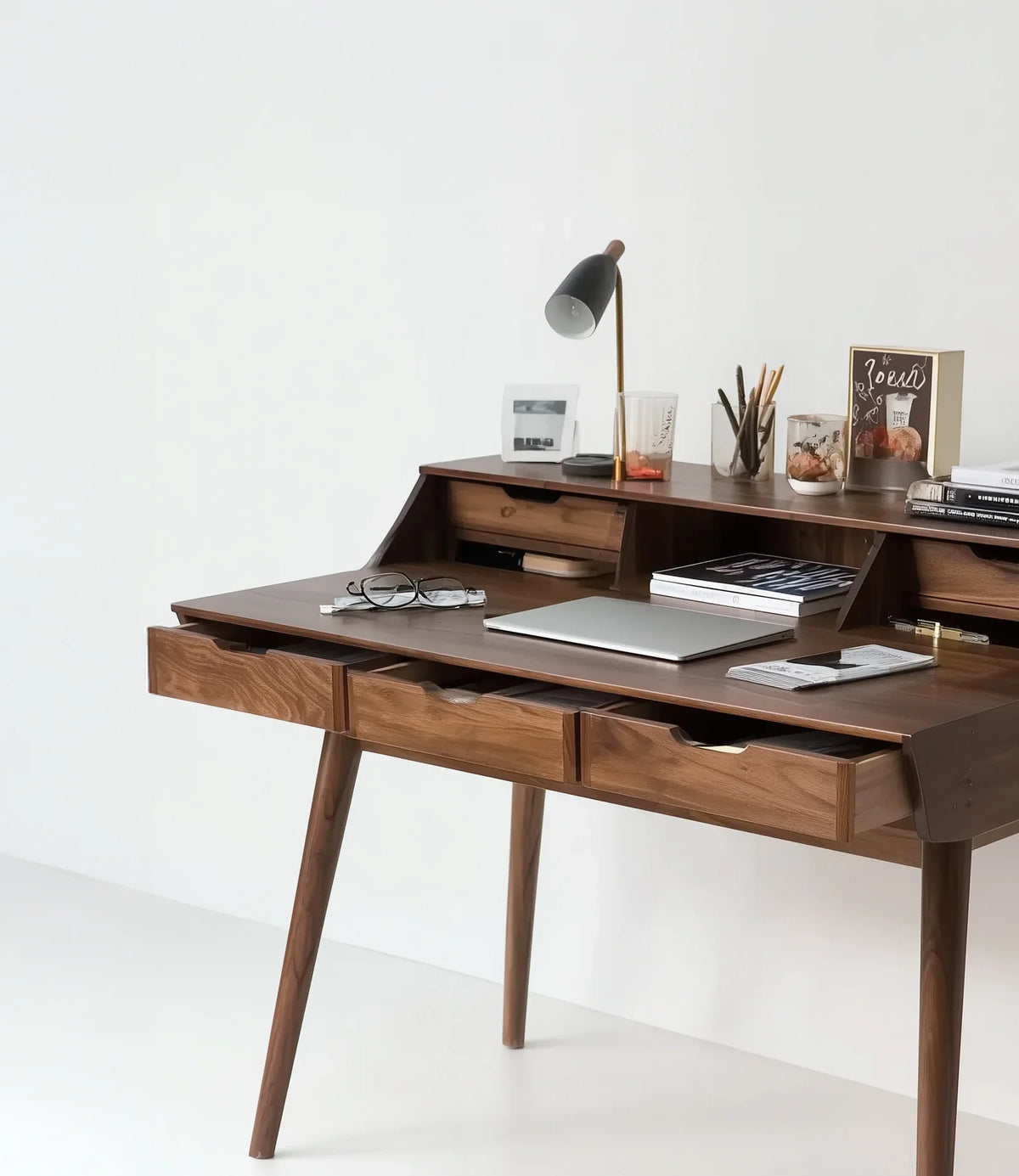 Solid wood writing desk with drawers, modern lamp, books, and workspace accessories