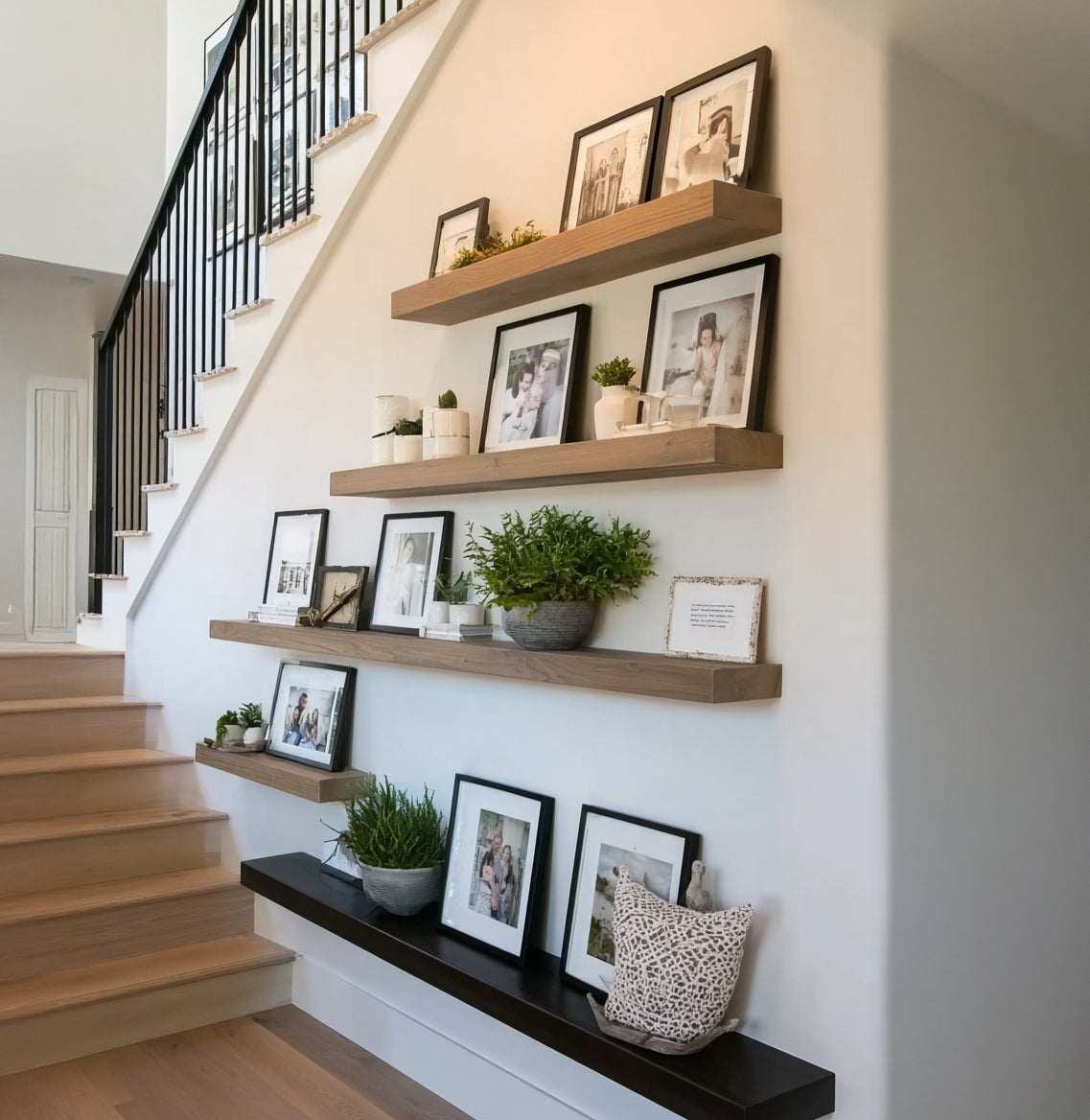 Modern home staircase with wooden floating shelves displaying framed family photos and green plants
