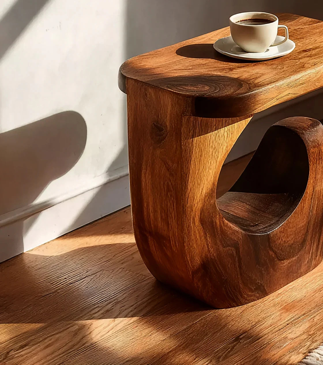 Natural wood side table with curved base and coffee cup in warm sunlight on wooden floor